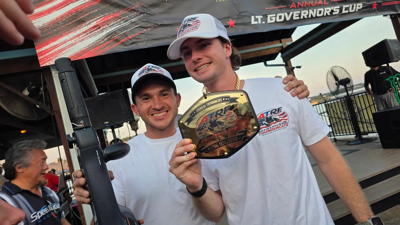 A smiling racer holds up a championship belt on the awards stage