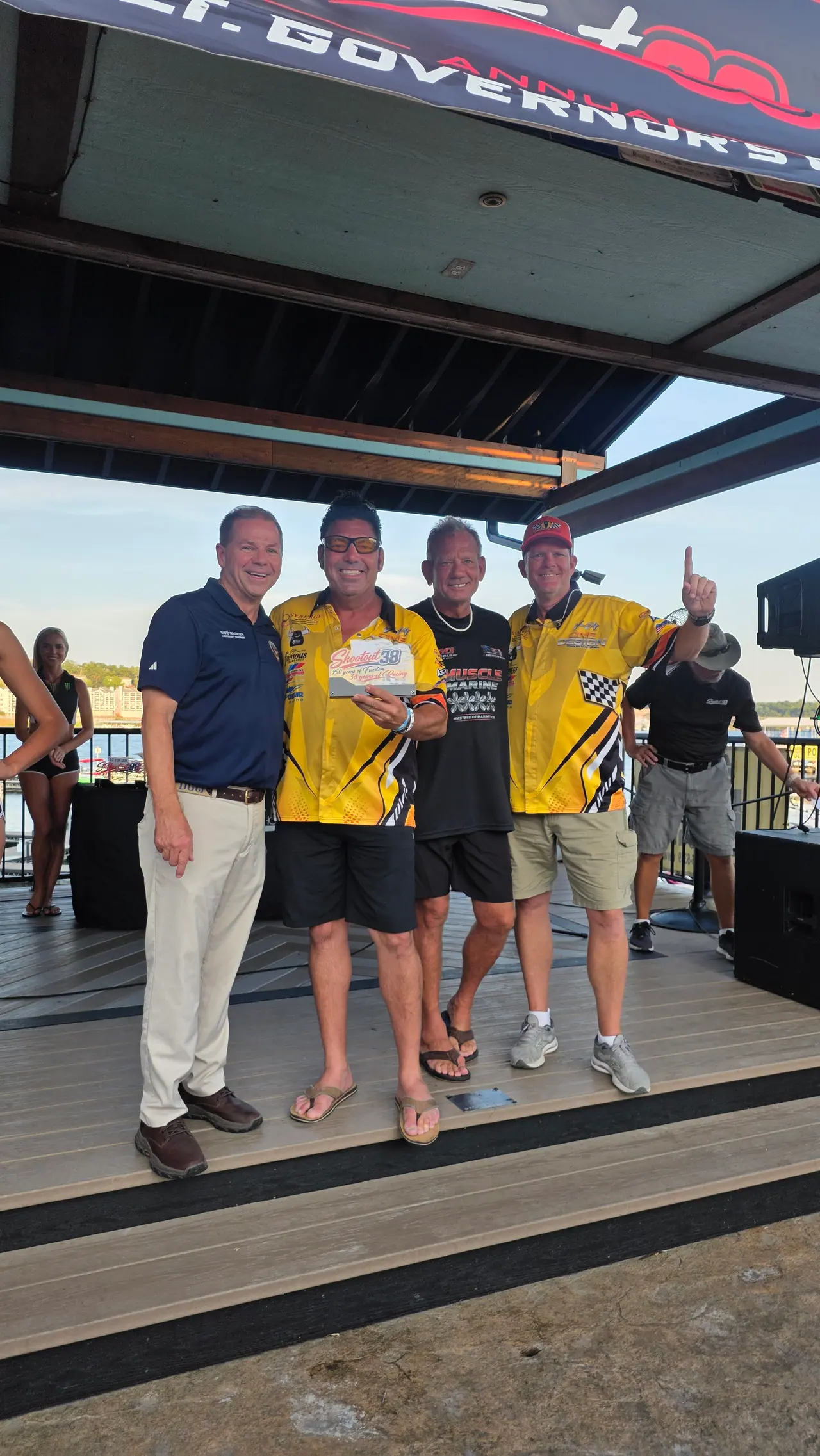 Racers in yellow team shirts holding trophies on the awards stage with an event official