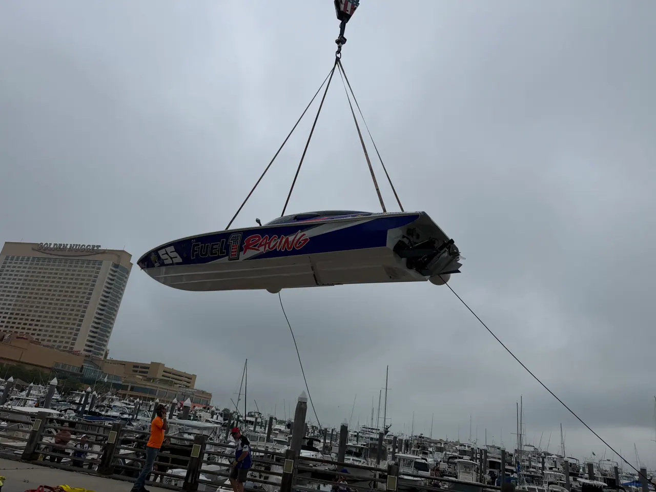 The #55 Fuel 1 Racing boat hanging from a crane above a marina, hotel towers behind it
