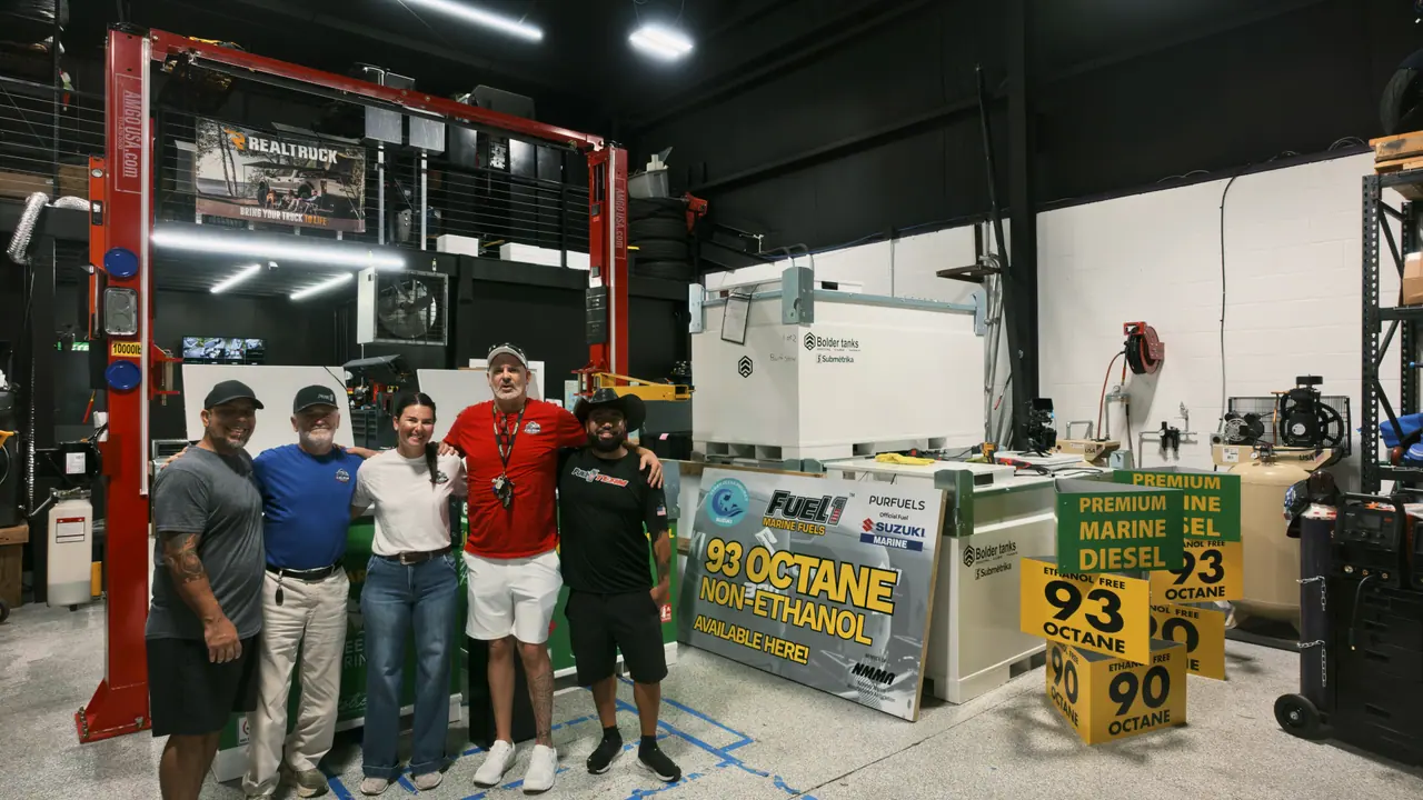 A group stands in a service shop beside 93 octane non-ethanol and premium marine diesel displays