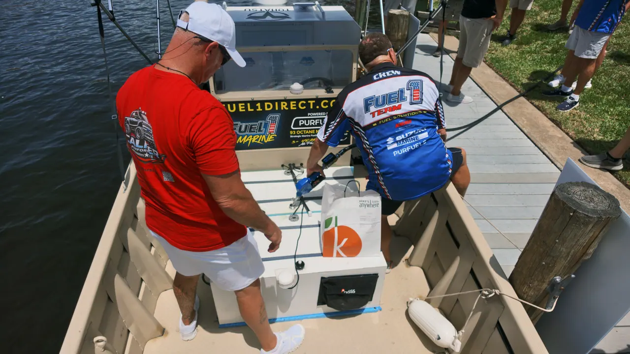 A crew member in a Fuel 1 Team jersey fueling a boat at a canal-side dock