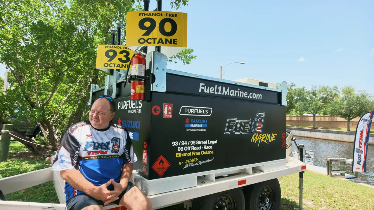 A team member sits beside the Fuel 1 Marine fuel trailer with ethanol-free 90 and 93 octane signs