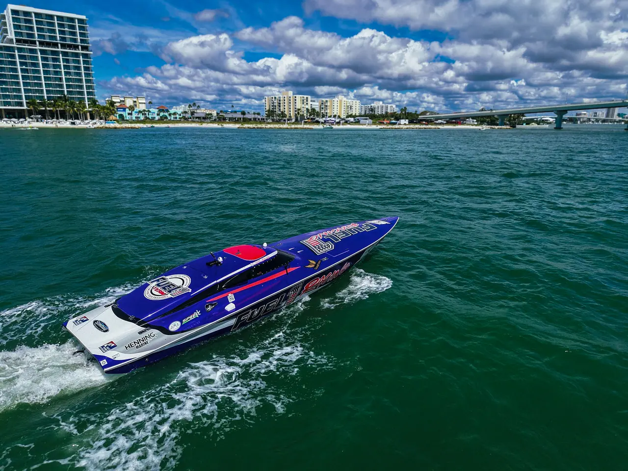The purple, white and red Fuel 1 Racing #55 Phantom running across green water off Clearwater Beach, hotels and the causeway behind