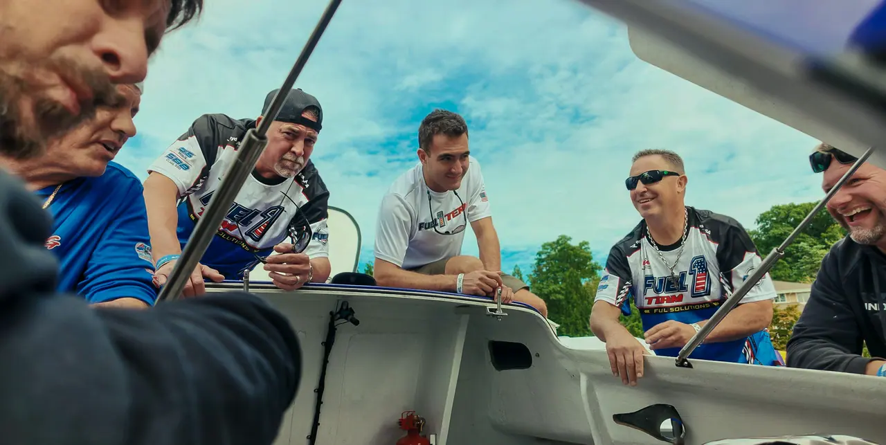 Crew members gathered around the open cockpit of the race boat, wide-angle view