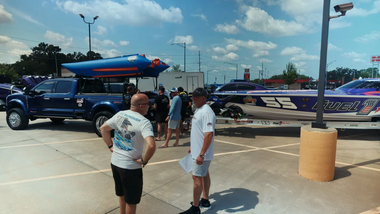 Fuel 1 crew members talking beside the team truck and the #55 boat in a sunny pit lot