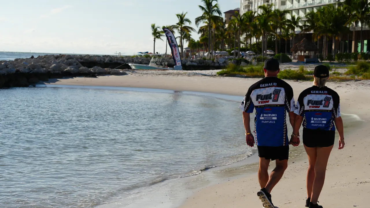Two team members in Fuel 1 jerseys walking along a quiet beach toward palm trees