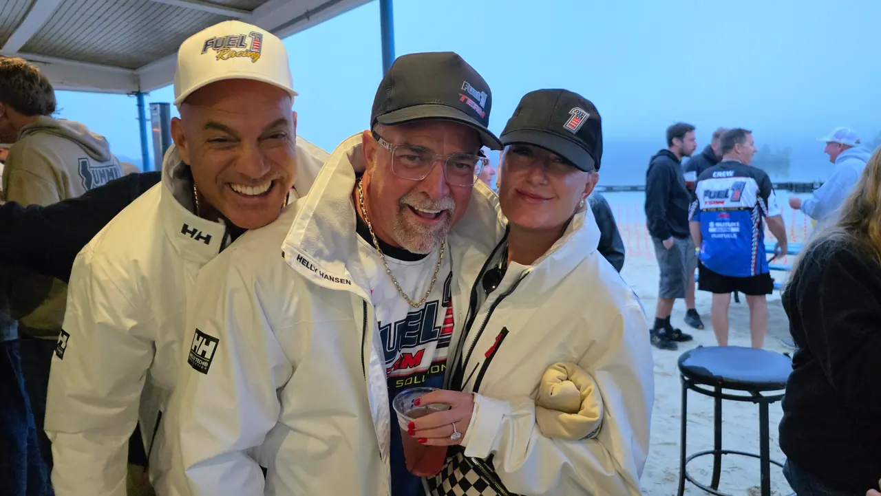 Three people in Fuel 1 gear and white race jackets smiling for a photo at the lakeside party